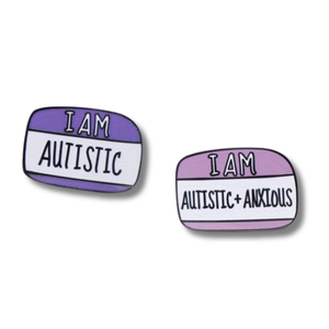 Two enamel pins with text 'I AM AUTISTIC' and 'I AM AUTISTIC + ANXIOUS' on a white background.