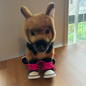 Plush toy resembling a dog with pink shoelaces on a wooden surface