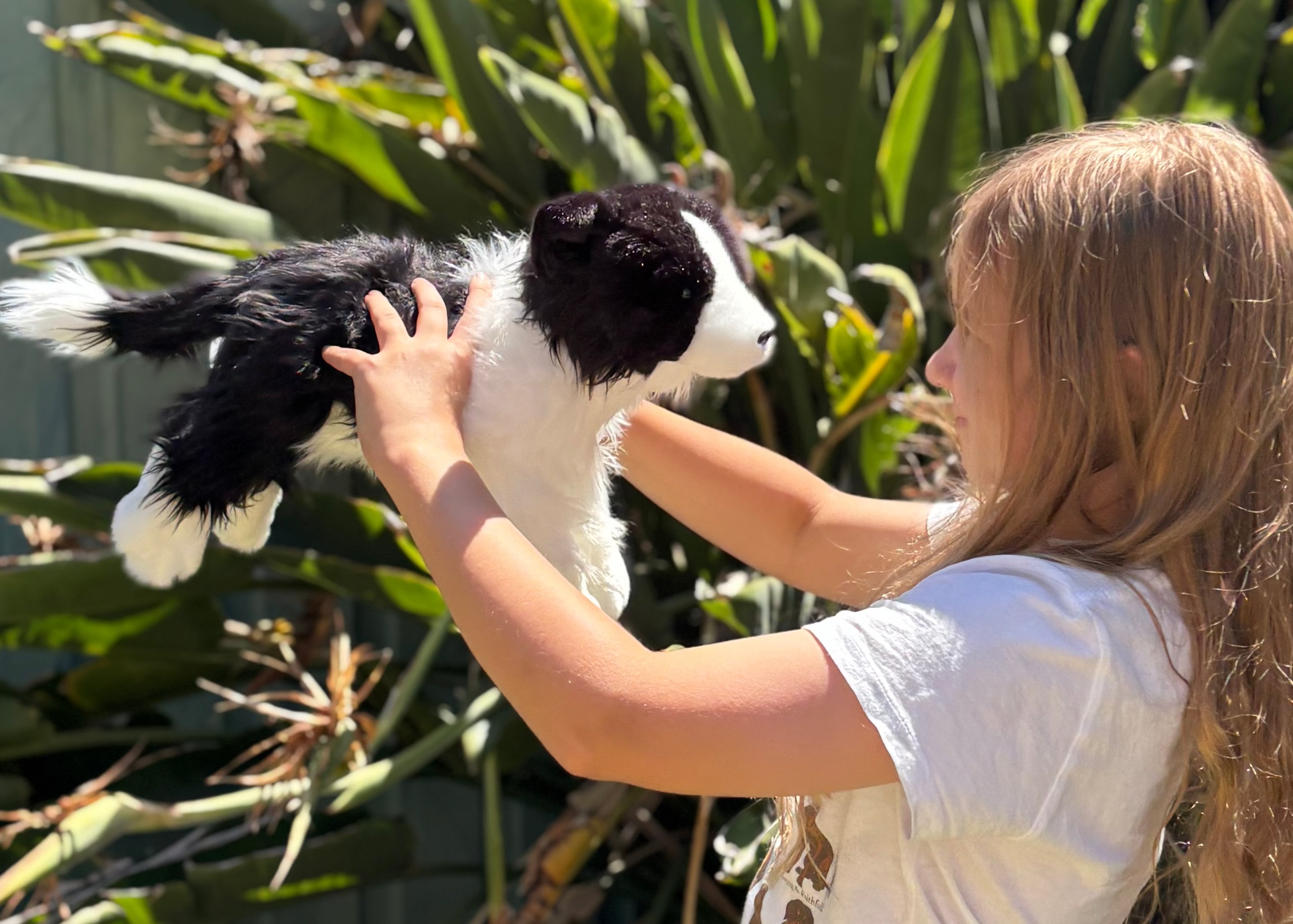 A girl holding a border collie plush dog up in the air