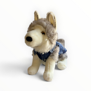A plush toy dog styled like a husky, sitting and wearing a small denim vest, photographed on a clean white background.