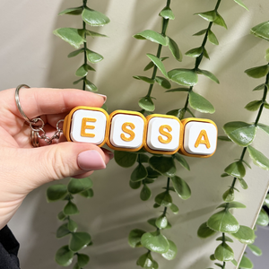 Keychain with 'ESSA' letters held by a hand in front of green leaves