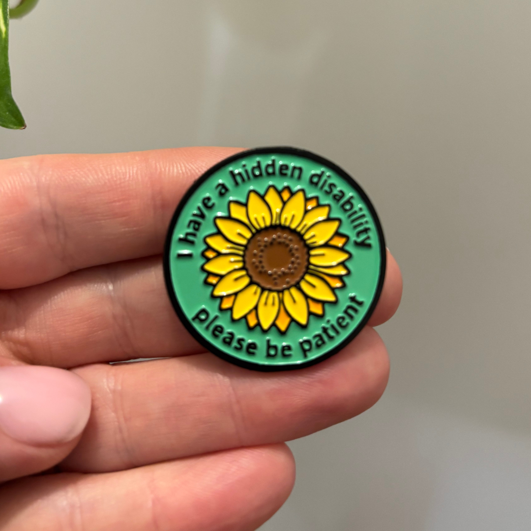Round green badge with sunflower design held in a hand, featuring text about a hidden disability.
