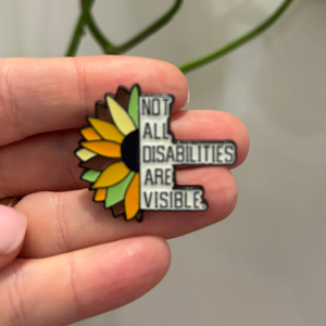 Pin with sunflower design and text 'Not all disabilities are visible' held in a hand.
