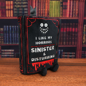Black plush bag with text and a ghost face design on a wooden surface with bookshelf background