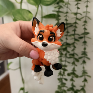 Hand holding a small fox figurine with green plants in the background