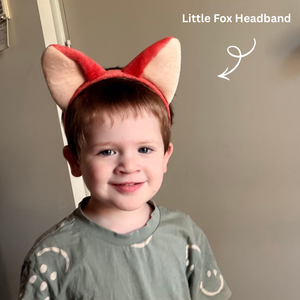 Child wearing a red fox headband with a plain background