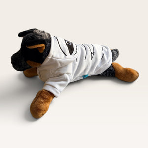 A plush Rottweiler dog toy wearing a white hoodie with black graphic details, posed on a light beige studio background.