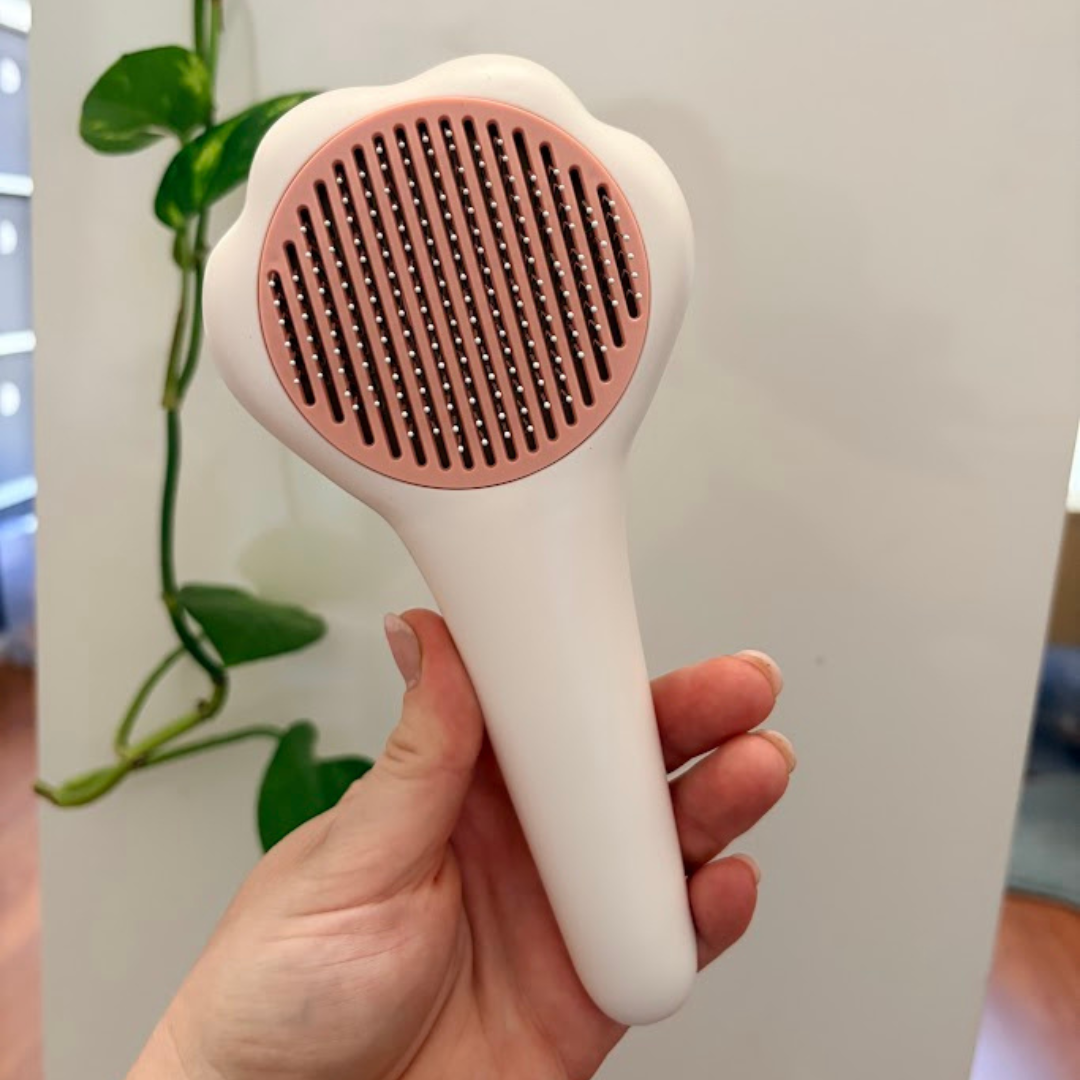White and pink pet grooming brush held in a hand with a plant in the background