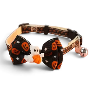 A Halloween-themed pet collar with a large black bow decorated with orange pumpkins, white stars, and a small white ghost holding an orange pumpkin. The collar itself has a pumpkin print pattern and features a small bell on the side.