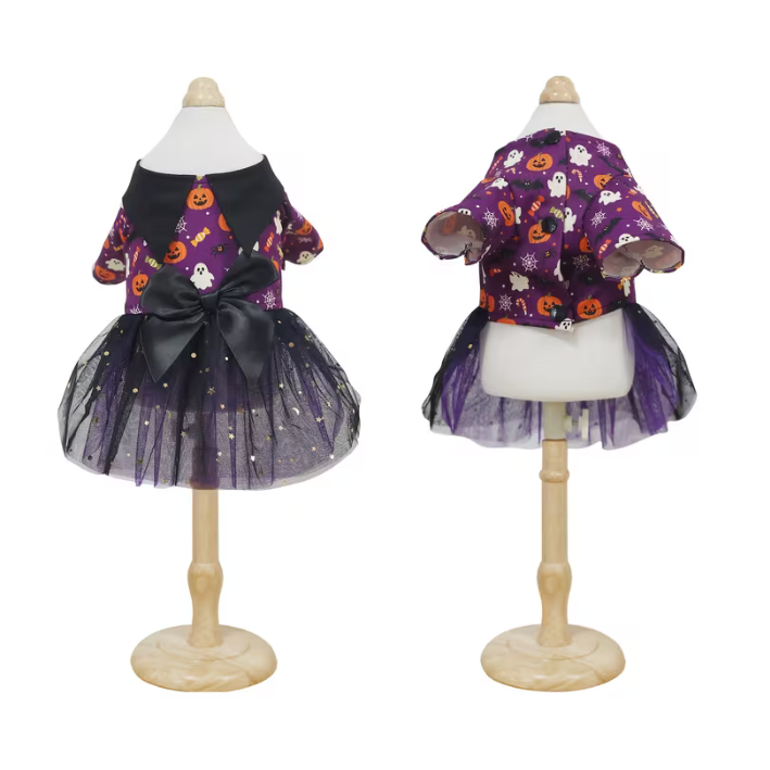 A pet's Halloween dress displayed on a mannequin from the front and back. The dress has a purple bodice with orange pumpkin prints, a purple tulle skirt with small gold star prints, and a large black bow at the waist.
