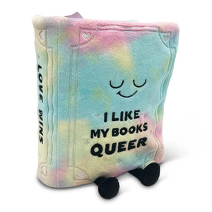 A plush book-shaped pillow with a pastel tie-dye design in pink, blue, yellow, and green. It features a simple embroidered smiling face and the text 'I LIKE MY BOOKS QUEER' on the front, with 'LOVE WINS' printed vertically on the spine.