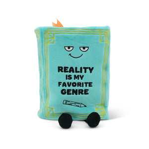 Plush toy book with text 'Reality is my favorite genre' on a white background