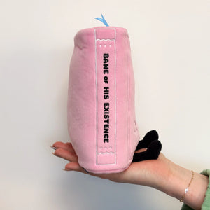 Pink plush toy with 'Bane of His Existence' text held in a hand against a light background