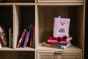 Stack of books with a pink book featuring text on a wooden shelf.
