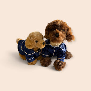 Two plush dog toys wearing matching navy blue pajamas with white piping, posed together on a plain warm beige background.