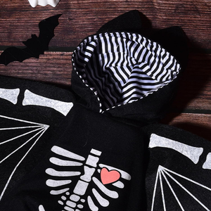 Black cat-ear hoodie with a white skeleton rib cage graphic and a pink heart on the chest, laid flat on a dark wood background with a black bat decoration.