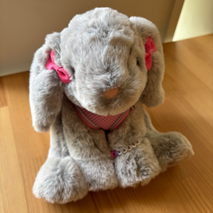 Plush toy dog with a pink bow on a wooden surface