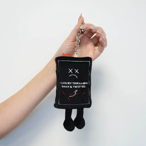 Black plush keychain with text and a sad face held by a hand against a white background