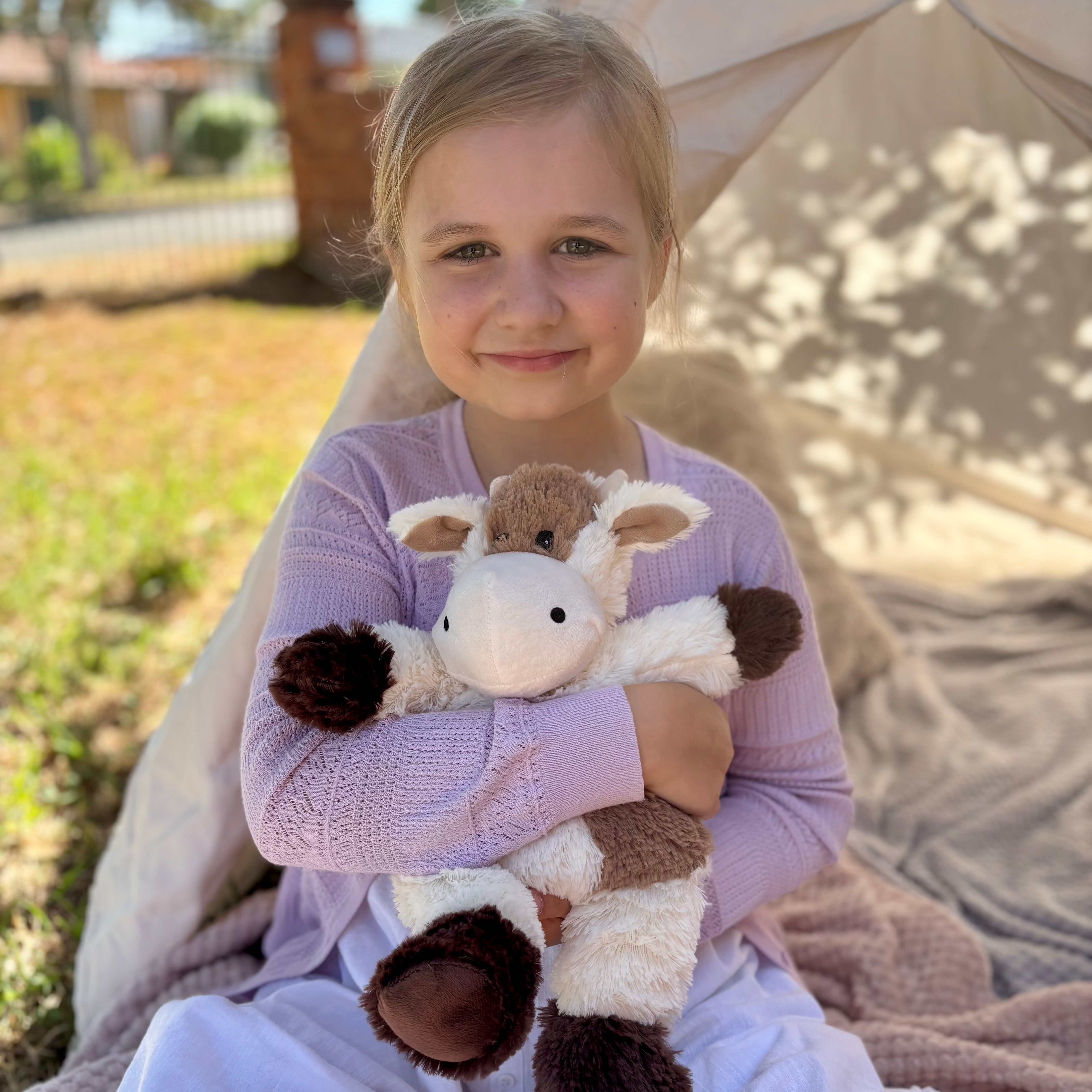 girl holding a Cow plushie - Warmies brand - weighted, lavender scented heat bag