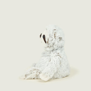 A plush sloth toy in white and light gray faux fur, sitting in profile against a solid, warm off-white background.