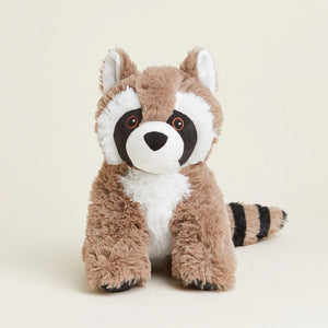 A plush raccoon toy sitting upright, made of soft brown and white faux fur with black-and-white facial markings and a black-and-white striped tail, photographed on a clean warm off-white studio background.