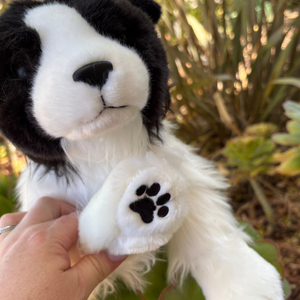 Plush toy dog held by a hand with a blurred natural background