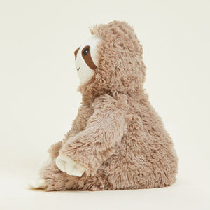 A plush sloth toy sitting in profile, featuring shaggy light brown fur, a white face, and dark brown facial details, photographed against a clean off-white background.