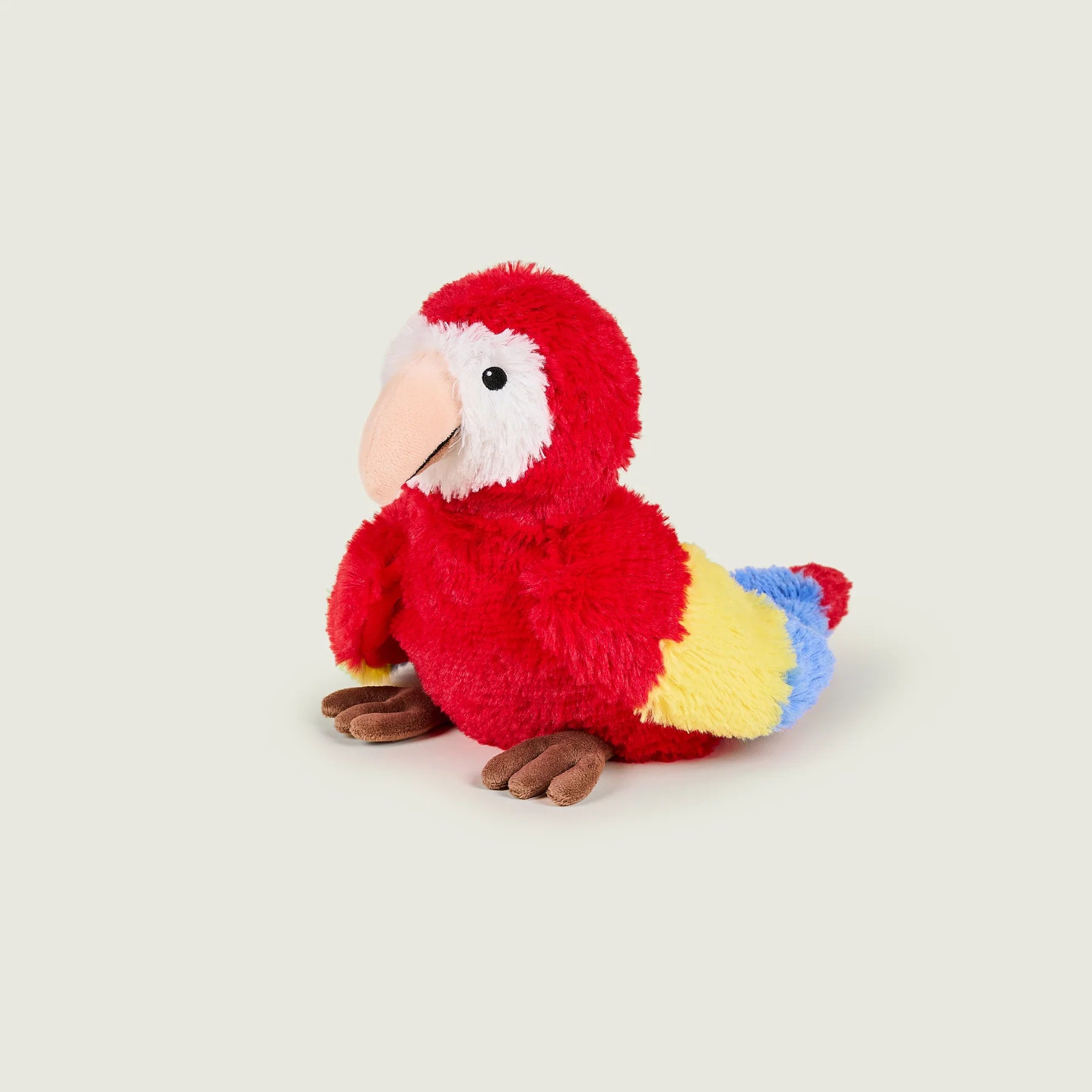 A plush toy parrot with bright red fur, a white face patch, a peach beak, and yellow, blue, and brown accents, photographed on a plain light gray background.