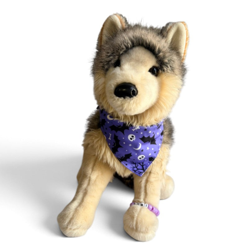 A plush dog toy wearing a purple Halloween bandana with a black bat pattern, posed against a clean white background.