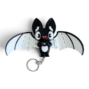 A black and white bat-shaped keychain charm with large cartoon eyes, a small metal key ring, and wing puzzle-piece details, shown on a plain white background.
