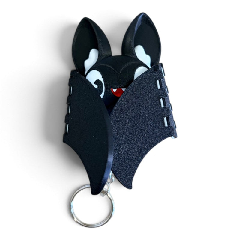 A black bat-shaped keychain with white accents and a silver metal key ring, shown on a plain white background.