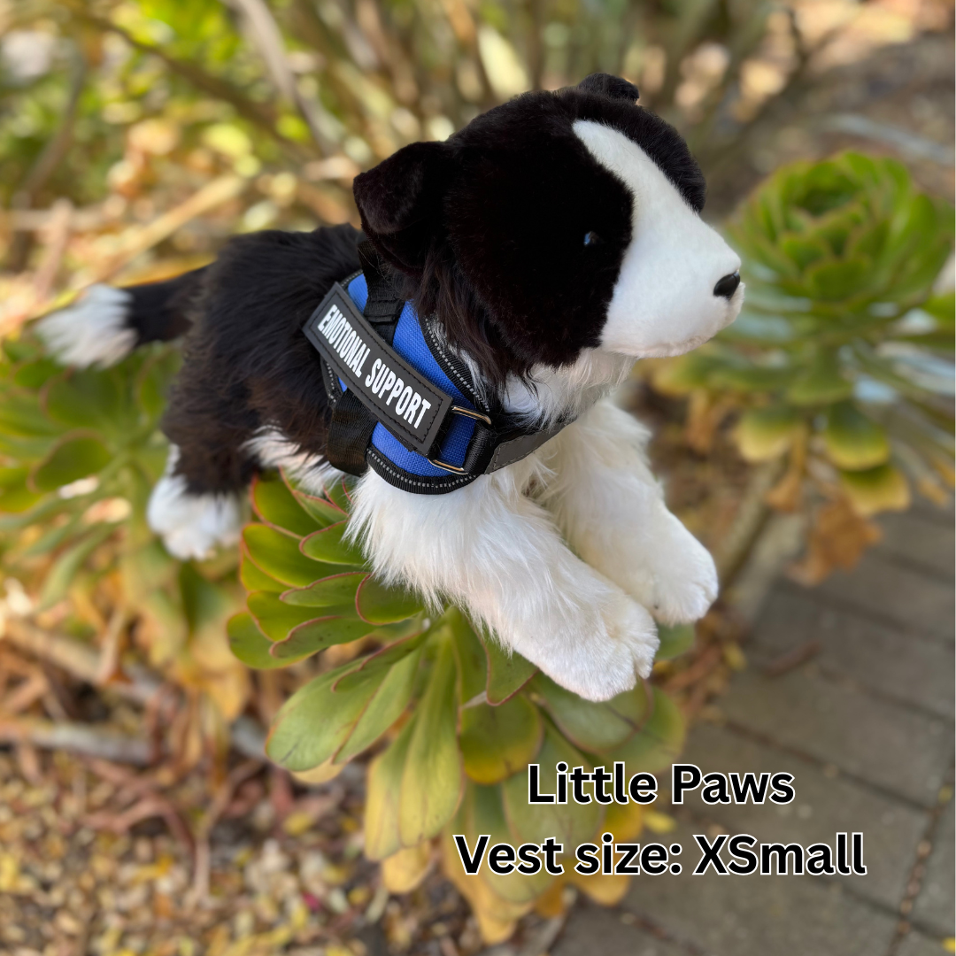 Black and white stuffed dog toy with a blue vest labeled 'Little Paws' on green plants.