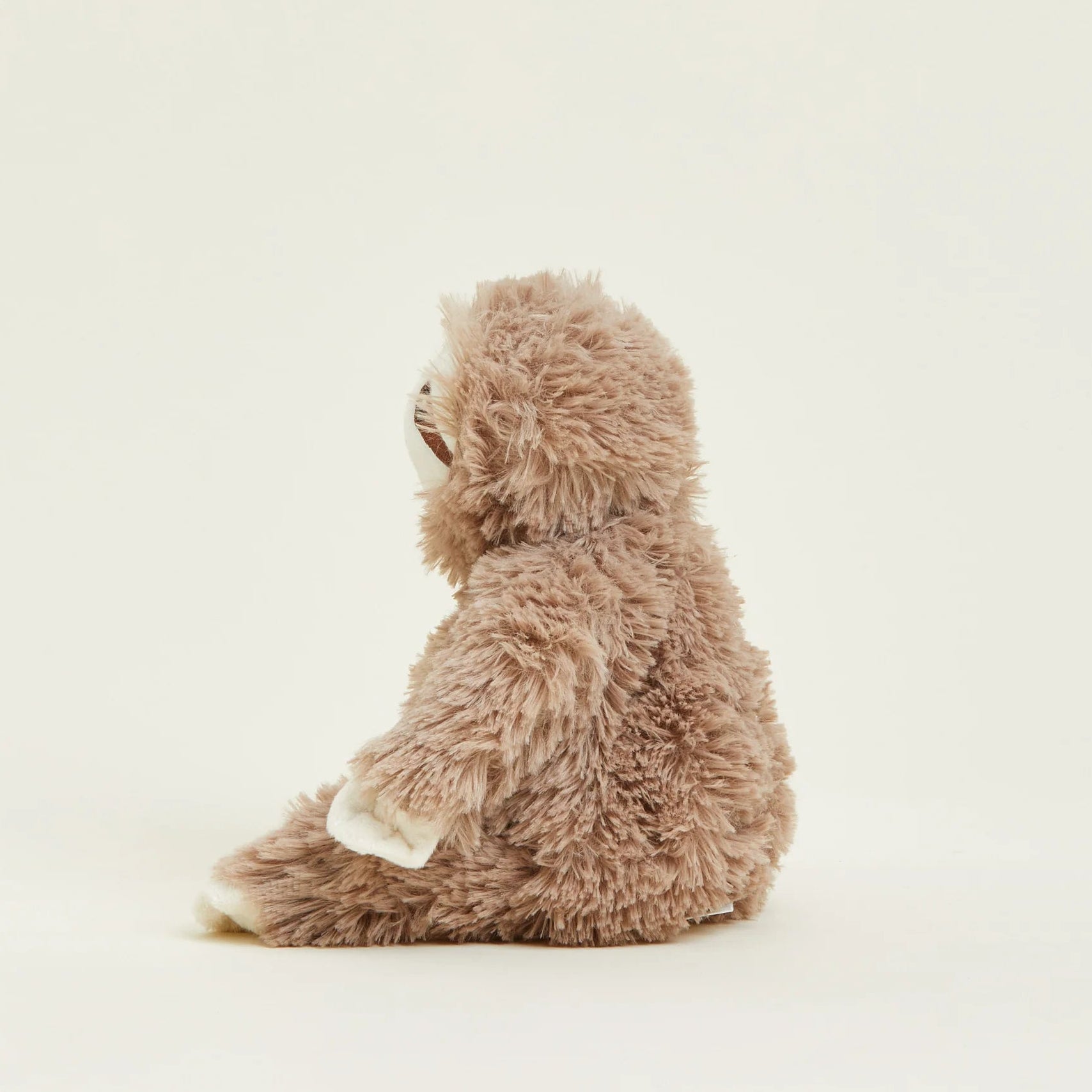 A plush sloth toy in a warm taupe-brown color with white accents on its paws and mouth, sitting on a plain off-white background.