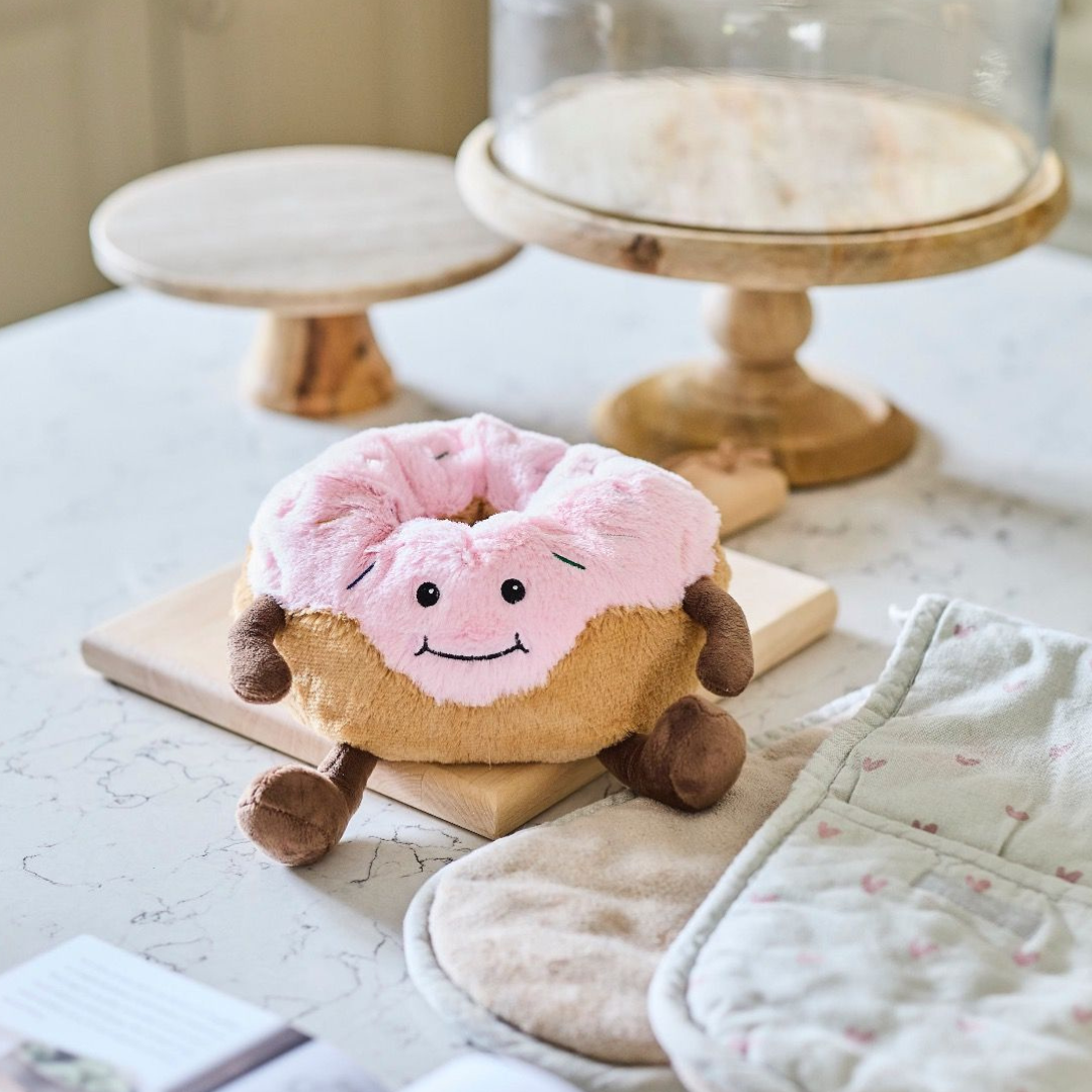 Plush donut toy with pink icing and brown feet on a light surface.