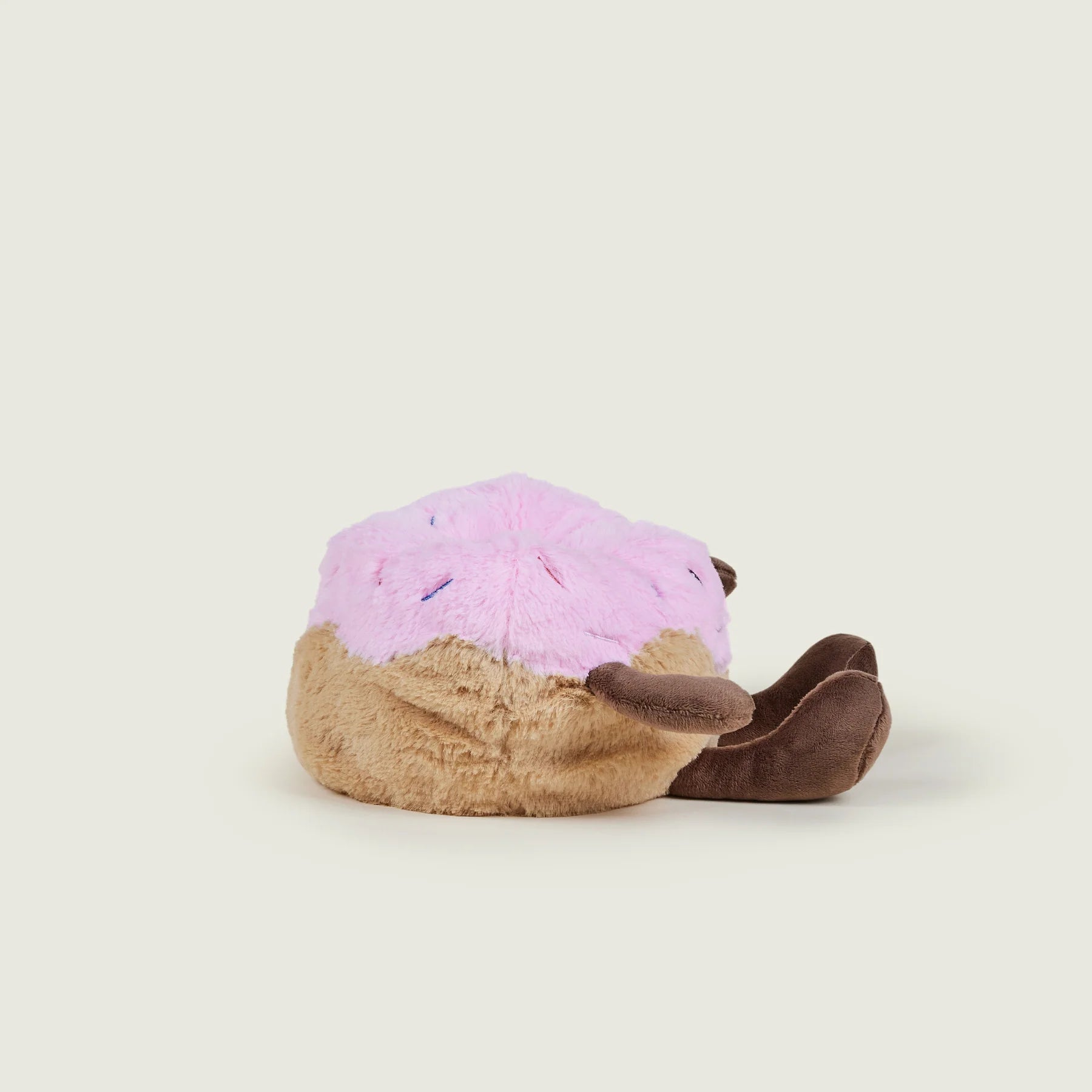 A plush donut-shaped slouchy pillow with pink frosting and brown filling, resting on a light beige background.