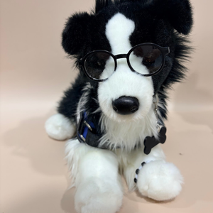 Stuffed toy dog with glasses and a bow tie on a beige background