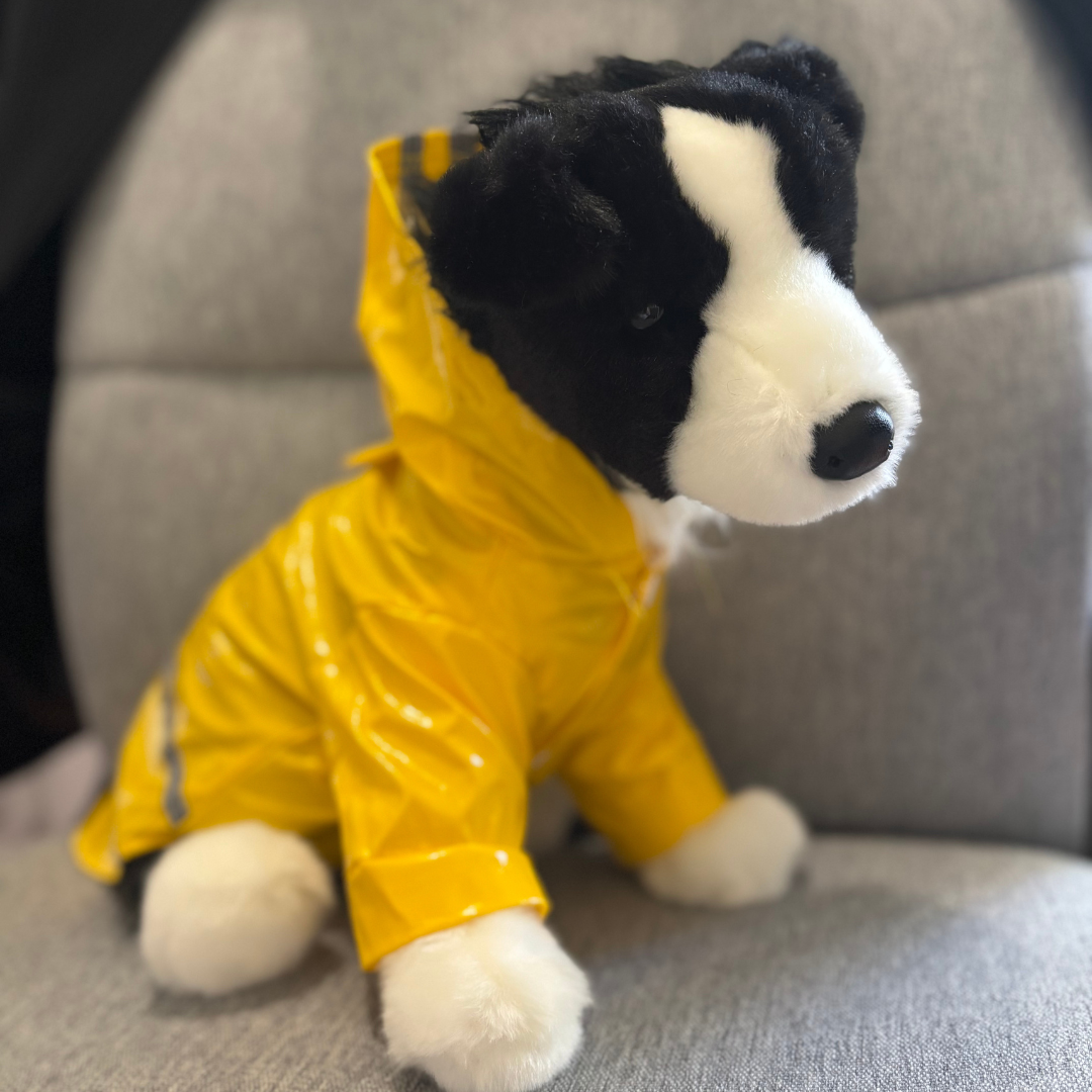 Plush toy dog in a yellow raincoat sitting on a gray surface.