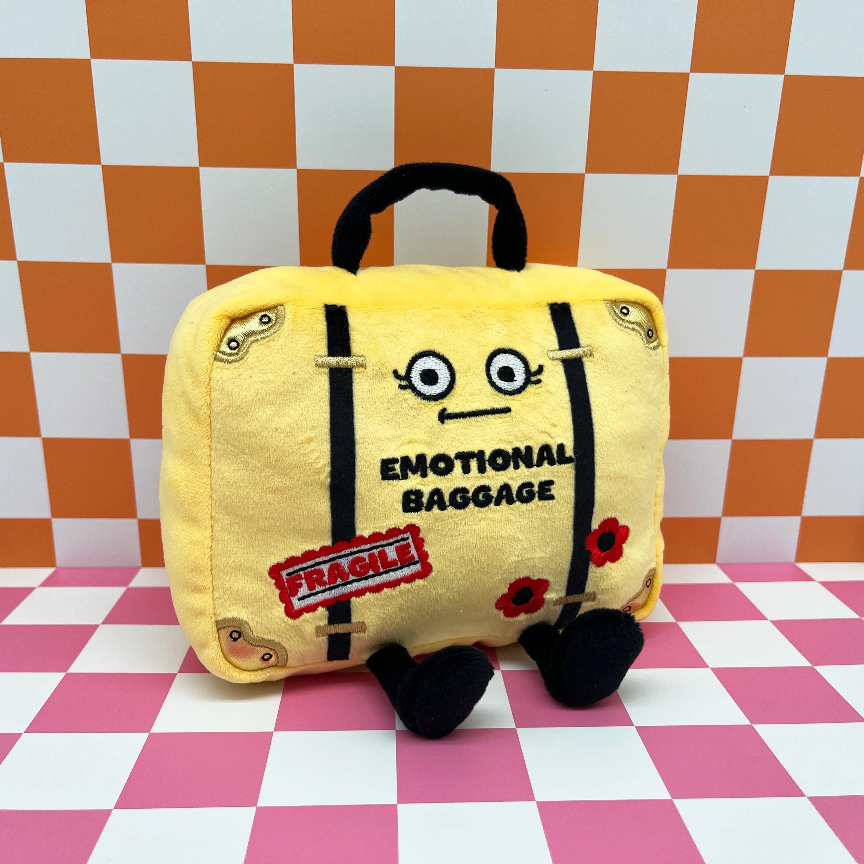 Plush toy suitcase labeled 'Emotional Baggage' on a checkered background