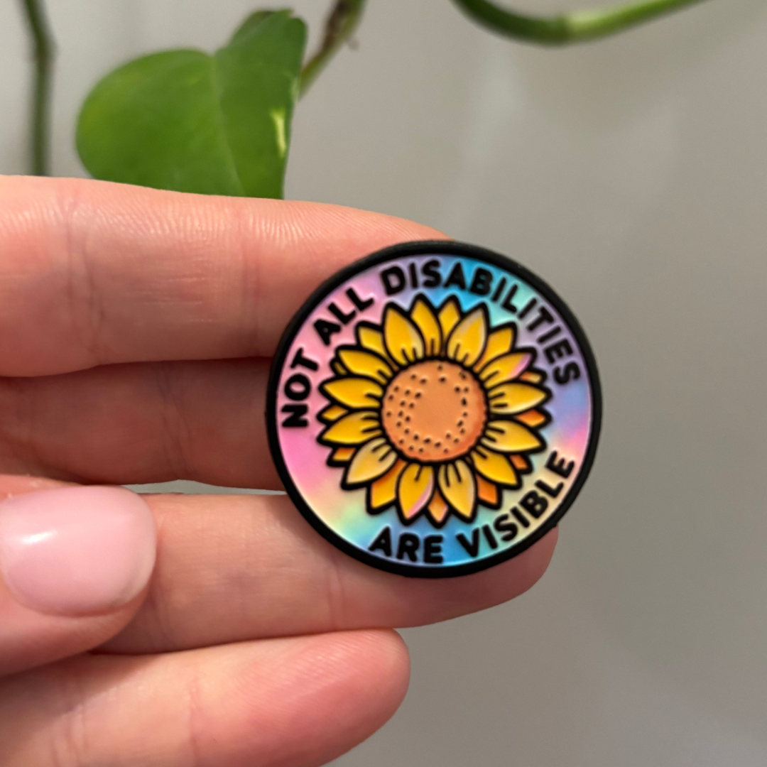 Round sticker with sunflower design and text 'Not all disabilities are visible' held by a hand.