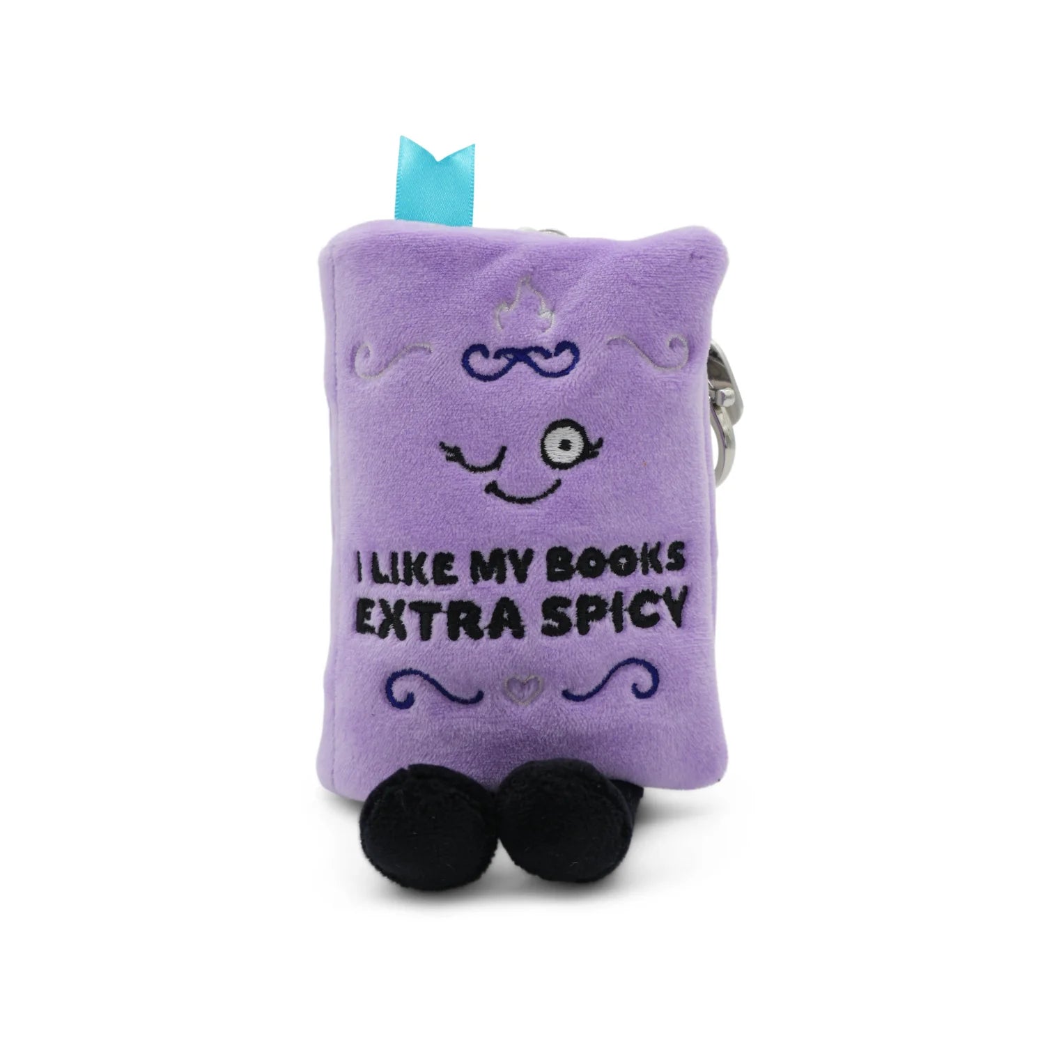 A purple plush book-shaped keychain or pouch with embroidered details, including a smiling face, the text 'I LIKE MY BOOKS EXTRA SPICY', black feet, and a small light blue ribbon at the top, shown on a white background.