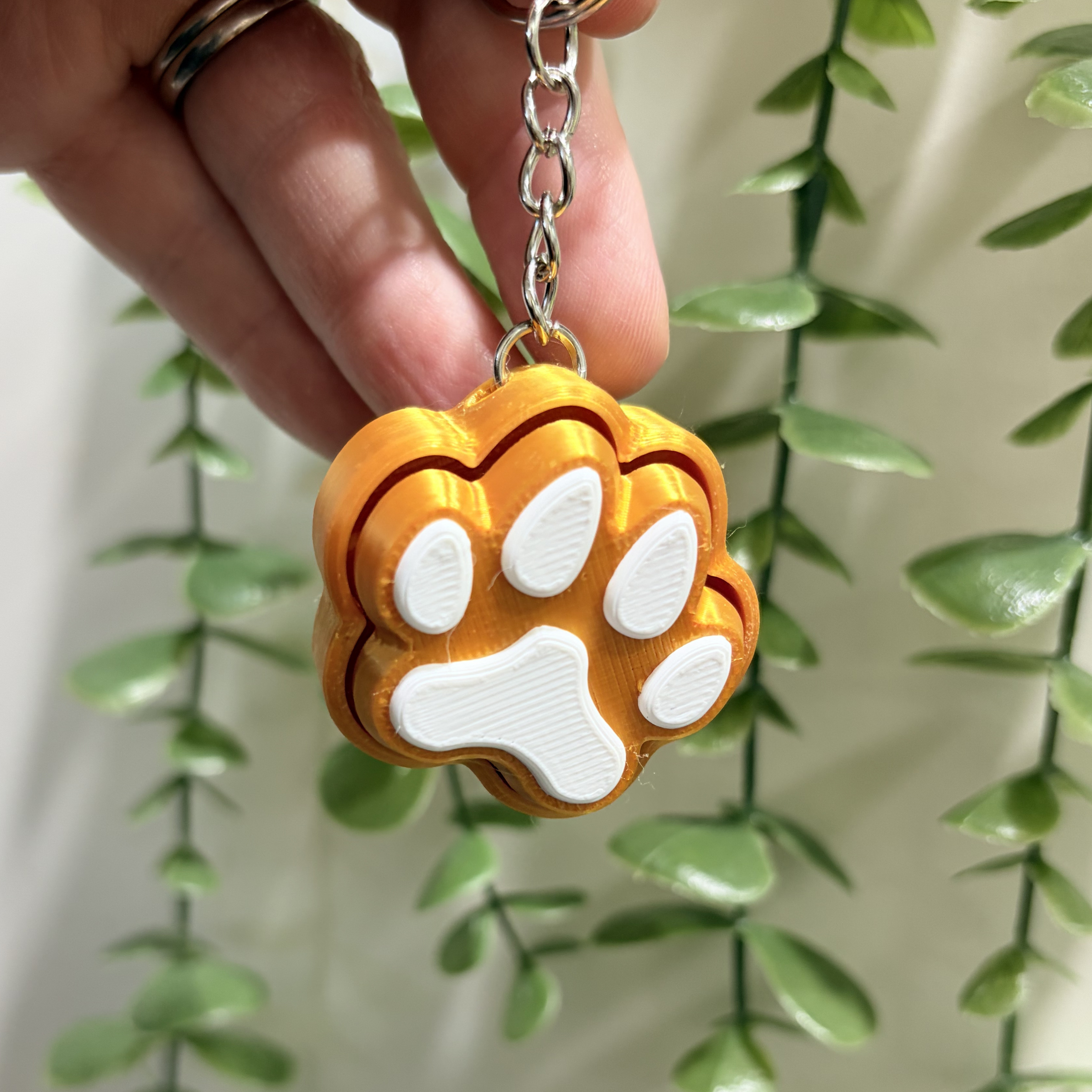 Gold keychain with a white paw print held by a hand against a green leafy background