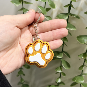 Hand holding a keychain with a paw design against a green leafy background
