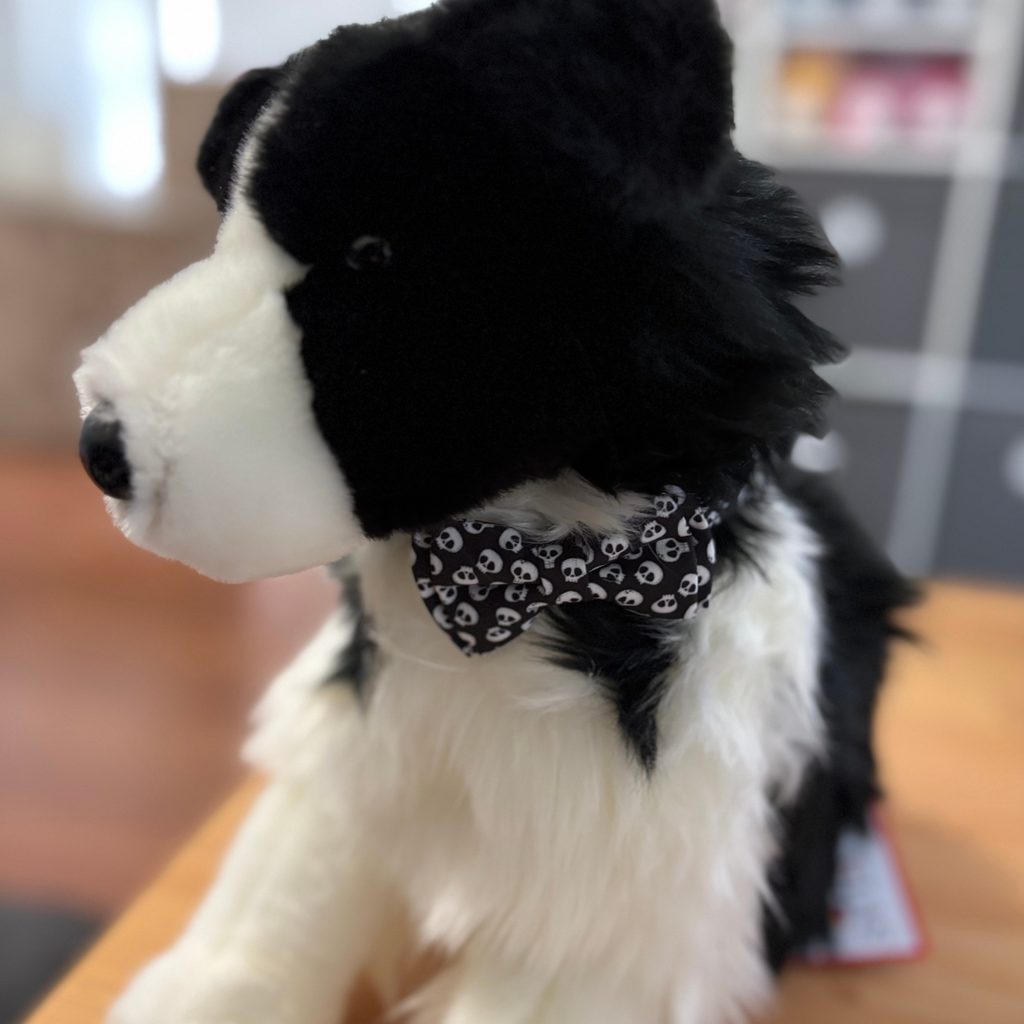 Black and white stuffed dog toy with a skull patterned bandana on a wooden surface.