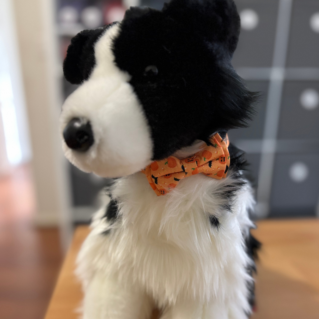 Stuffed dog toy with a black and white pattern and an orange bow tie on a wooden surface.