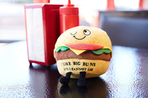Plush burger toy with a smiley face on a table with condiment bottles in the background.