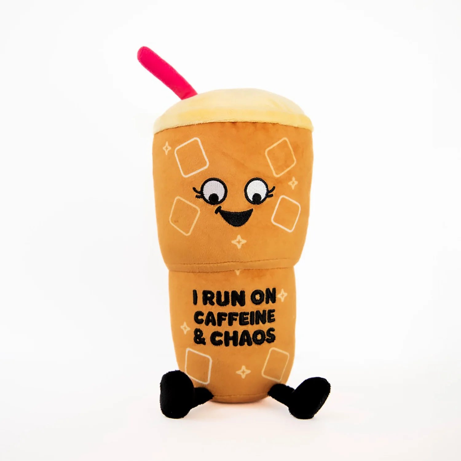 A plush toy shaped like a cartoon iced coffee cup with a smiling face, black text reading 'I RUN ON CAFFEINE & CHAOS', cream-colored foam top, black legs, and a pink straw on a white background.