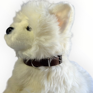 A close-up side profile of a fluffy white faux-fur dog toy wearing a dark brown collar with silver metal hardware, set against a plain white background.