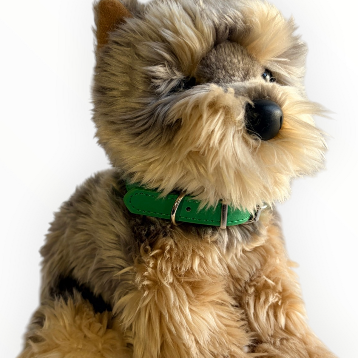A close-up of a fluffy dog toy or plush dog with tan and gray fur, wearing a bright green collar, photographed against a plain white background.