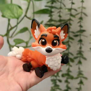 Toy fox figure held in a hand with a plant in the background