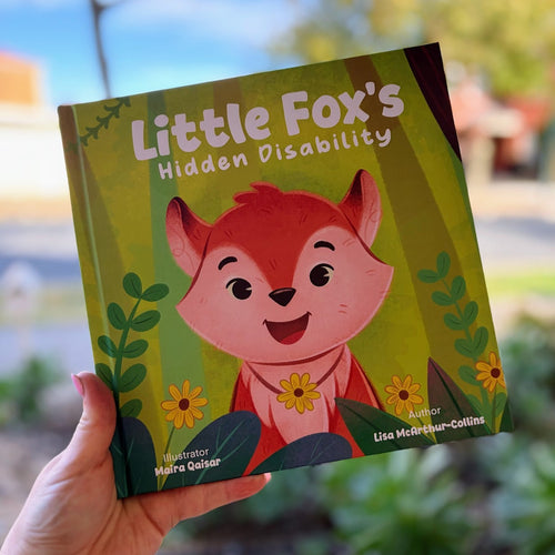 Book titled 'Little Fox's Hidden Disability' held by a person outdoors.